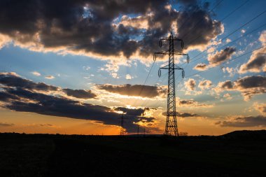 Güzel dramatik gökyüzü ve bulutlar, gün batımının ışıkları iletim kulesinin üzerinde (elektrik direği) bir tarlada.