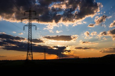Güzel dramatik gökyüzü ve bulutlar, gün batımının ışıkları iletim kulesinin üzerinde (elektrik direği) bir tarlada.