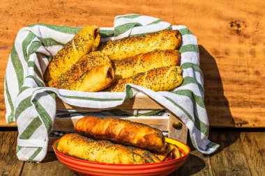 Hamurda pişmiş sosisler tuzlu ve haşhaş tohumlarıyla dolu kırsal bir sepetin içinde. Sosisli börekler, ev yapımı lezzetli hamur işleri..