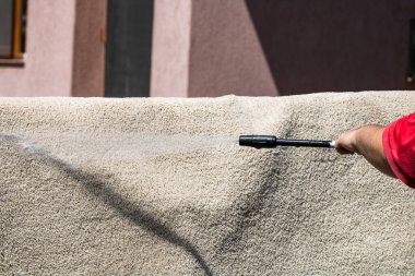 Yüksek basınçlı çamaşır makinesiyle halıları yıkayın. Yüksek basınçlı suyu yıkamak için halıyı silahla temizlemek. Ev temizliği kavramı.