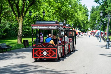 Çocuklu aileler parkta trenle geziyorlar. 2020 yılında Romanya 'nın Bükreş kentindeki Mogosoaia kentinden insanlar park ve bahçelerde yürüyor, dinleniyor ve eğleniyorlar..