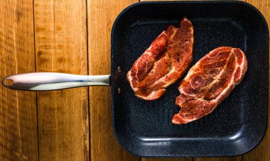 Baharatlı domuz pirzolası ve siyah bir tavada füme sosis, ahşap masa üzerinde, bbq için et, üst manzara, fotokopi alanı, barbekü konsepti