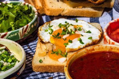 Sosisli börek, kızarmış yumurta, kızarmış ekmek, soslu farklı kaseler ve doğranmış sebzeler..