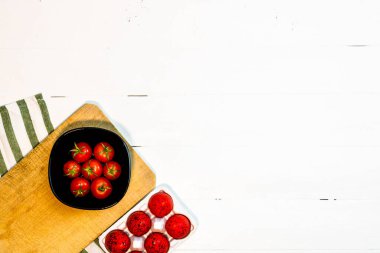 Taze kiraz domatesleri ve kırsal beyaz ahşap bir masada kırmızı paskalya yumurtaları. Malzemeler ve gıda konsepti