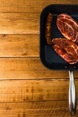 Baharatlı domuz pirzolası ve siyah bir tavada füme sosis, ahşap masa üzerinde, bbq için et, üst manzara, fotokopi alanı, barbekü konsepti