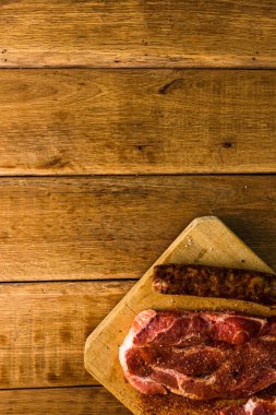 Baharatlı domuz pirzolası ve ahşap bir tahta kesme tahtasında tütsülenmiş sosis, bbq için et, üst manzara, fotokopi alanı, barbekü konsepti