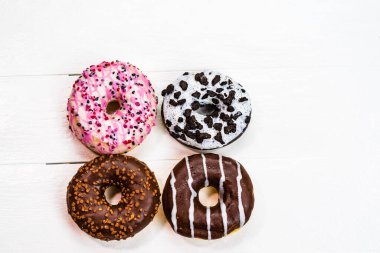 Beyaz ahşap masada renkli çörekler. Şekerli, şekerli, şekerli, şekerli, şekerli. Kopyalama alanı olan üst görünüm