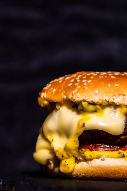 Erimiş peynirli sığır eti çizburgerinin ayrıntıları siyah arka planda izole edilmiş..