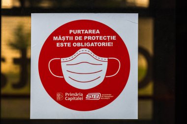 STB otobüsünün kapılarında Rumen metni, cerrahi maske takmalısın. Bükreş, Romanya, 2020.