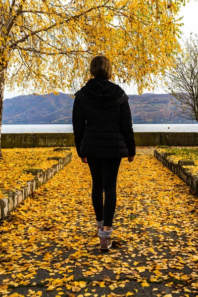 Autumn leaves fallen on alone woman walking on the autumn alley. Autumn landscape, orange foliage in a park in Orsova, Romania, 2020