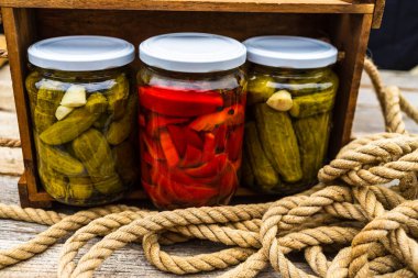 Ahşap sandıkta izole edilmiş turşulu kırmızı biberli cam kavanozlar ve salatalık turşusu. Çeşitli sebze turşulu kavanozlar. Kaba bir kompozisyonda yiyecek konseptini korudu.