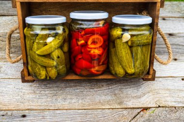 Ahşap sandıkta izole edilmiş turşulu kırmızı biberli cam kavanozlar ve salatalık turşusu. Çeşitli sebze turşulu kavanozlar. Kaba bir kompozisyonda yiyecek konseptini korudu.