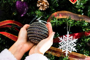 Noel ağacının önünde Noel süsü tutan eller. Noel süslemeleri ile köknar dallarını süslemek.