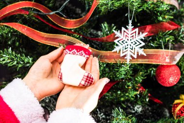 Noel ağacının önünde Noel süsü tutan eller. Noel süslemeleri ile köknar dallarını süslemek.