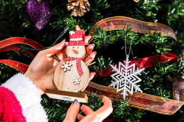 Noel ağacının önünde Noel süsü tutan eller. Noel süslemeleri ile köknar dallarını süslemek.