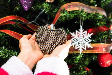 Noel ağacının önünde Noel süsü tutan eller. Noel süslemeleri ile köknar dallarını süslemek.