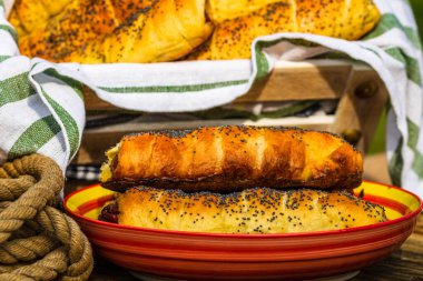 Hamurda pişmiş sosisler tuzlu ve haşhaş tohumları serpiştirilmiş, kırsal bir kompozisyonda. Sosisli börek, lezzetli ev yapımı hamur işleri..