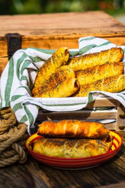 Hamurda pişmiş sosisler tuzlu ve haşhaş tohumları serpiştirilmiş, kırsal bir kompozisyonda. Sosisli börek, lezzetli ev yapımı hamur işleri..