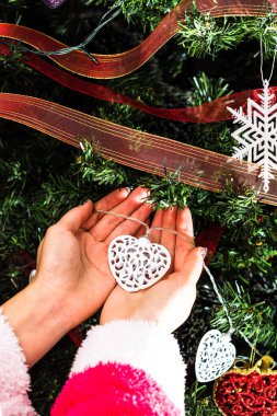 Noel ağacının önünde Noel süsü tutan eller. Noel süslemeleri ile köknar dallarını süslemek.