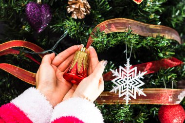 Noel ağacının önünde Noel süsü tutan eller. Noel süslemeleri ile köknar dallarını süslemek.