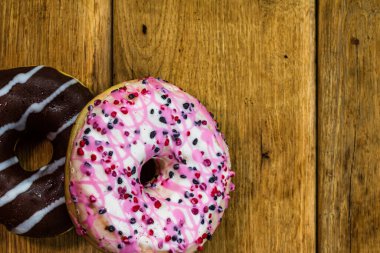 Ahşap masada renkli çörekler. Jöleli şekerli tatlı yiyecekler, çikolatalı donutlar. Kopyalama alanı olan üst görünüm