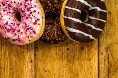 Ahşap masada renkli çörekler. Jöleli şekerli tatlı yiyecekler, çikolatalı donutlar. Kopyalama alanı olan üst görünüm