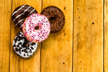 Ahşap masada renkli çörekler. Jöleli şekerli tatlı yiyecekler, çikolatalı donutlar. Kopyalama alanı olan üst görünüm