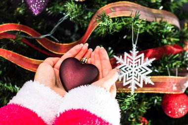 Noel ağacının önünde Noel süsü tutan eller. Noel süslemeleri ile köknar dallarını süslemek.