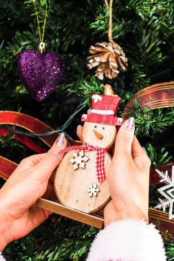 Noel ağacının önünde kardan adam heykelciği tutan eller. İzole edilmiş köknar ağacını süslemek