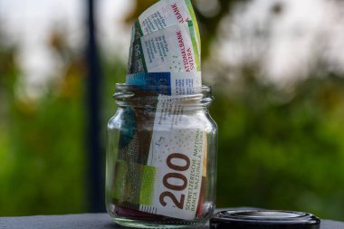 İsviçre frangı CHF banknotu cam kavanozda para biriktiriyor. Tüketim ve ekonomi. İş, bahşiş, finans, tasarruf, bankacılık ve insan kavramı