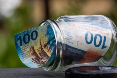 İsviçre frangı CHF banknotu cam kavanozda para biriktiriyor. Tüketim ve ekonomi. İş, bahşiş, finans, tasarruf, bankacılık ve insan kavramı