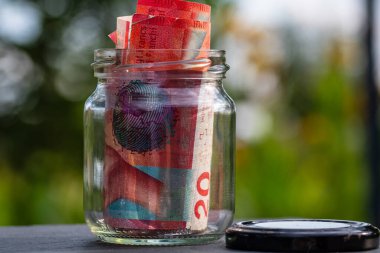 İsviçre frangı CHF banknotu cam kavanozda para biriktiriyor. Tüketim ve ekonomi. İş, bahşiş, finans, tasarruf, bankacılık ve insan kavramı