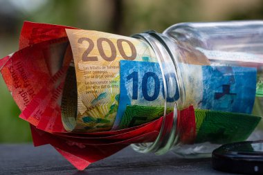 İsviçre frangı CHF banknotu cam kavanozda para biriktiriyor. Tüketim ve ekonomi. İş, bahşiş, finans, tasarruf, bankacılık ve insan kavramı