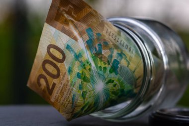 İsviçre frangı CHF banknotu cam kavanozda para biriktiriyor. Tüketim ve ekonomi. İş, bahşiş, finans, tasarruf, bankacılık ve insan kavramı