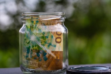 İsviçre frangı CHF banknotu cam kavanozda para biriktiriyor. Tüketim ve ekonomi. İş, bahşiş, finans, tasarruf, bankacılık ve insan kavramı