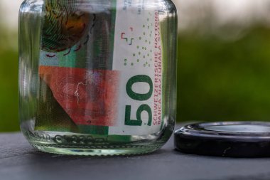 İsviçre frangı CHF banknotu cam kavanozda para biriktiriyor. Tüketim ve ekonomi. İş, bahşiş, finans, tasarruf, bankacılık ve insan kavramı