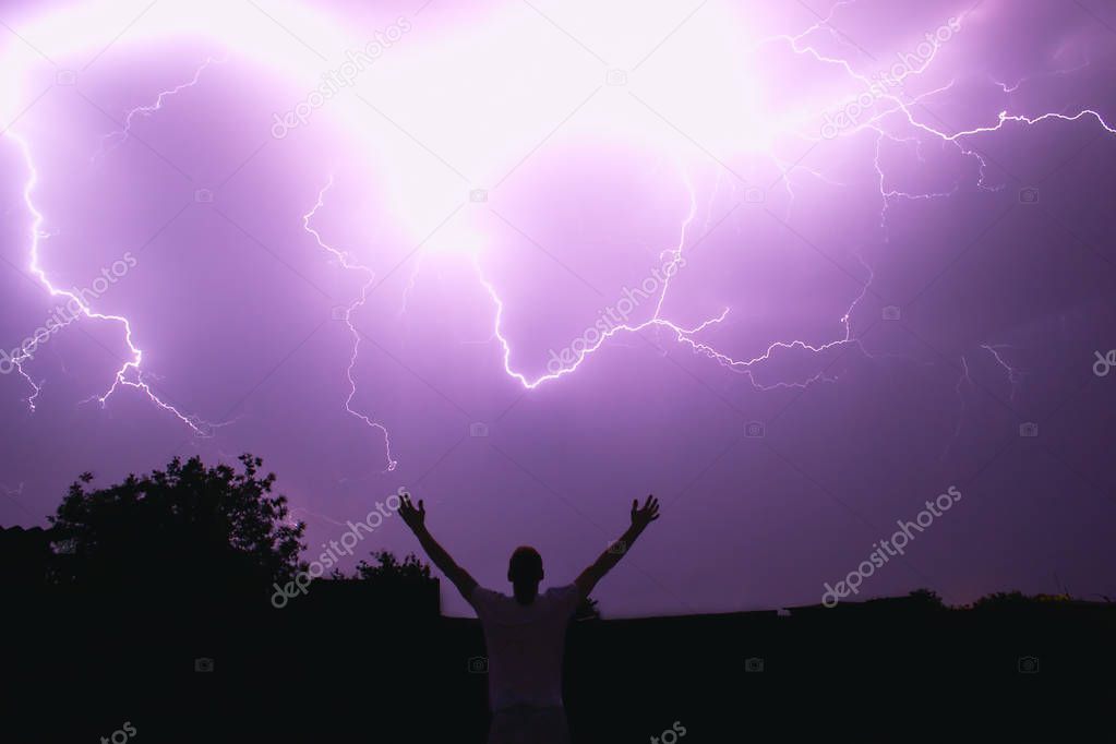 silhouette of the man of the magician summoning the lightning illuminating the night sky with bright flashes, the riot of the natural elements