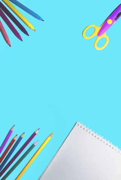 flat lay picture of colored pencils, notepad and scissors lined on a flat surface of an isolated blue background