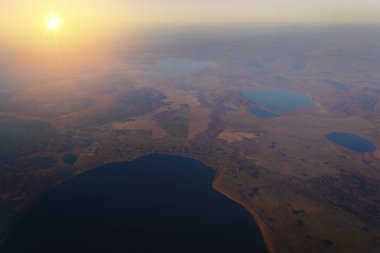 Güneş ışınları tarafından yaktı gün batımında göl ve nehir orman ile dağlarda ufku için uçak penceresinden görüntüleyin
