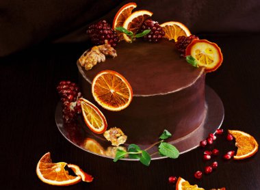 koyu kahverengi bir arka plan üzerinde nane bir sprig ile pişmiş portakal ve taze nar dilimleri ile dekore muhteşem çikolatalı kek