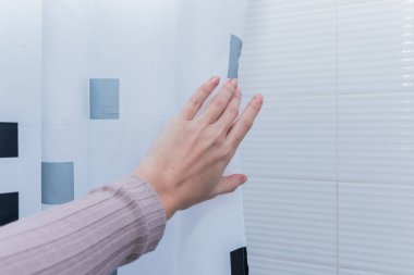 Beyaz banyoda duş perdesi tutan el.