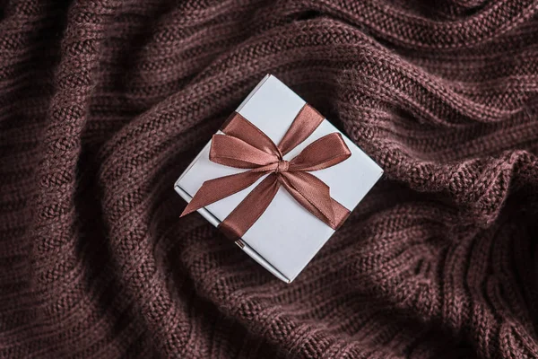 Pequeña caja de regalo con cinta marrón en manta marrón de punto cálido . —  Fotos de Stock