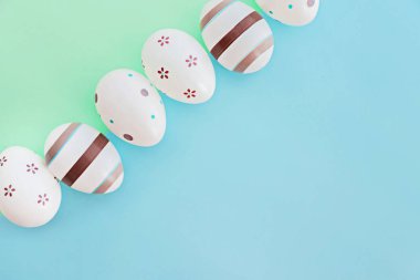 Yeşil ve mavi arka planda çizgili yumurta ve çiçeklerle süslenmiş Paskalya konsepti. Üst görünüm.