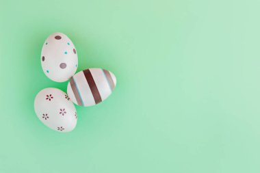 Yeşil arka planda çizgili yumurta ve çiçeklerle süslenmiş Paskalya konsepti. Üst görünüm.