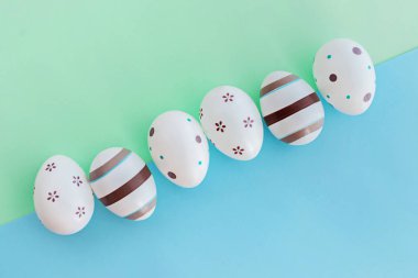 Yeşil ve mavi arka planda çizgili yumurta ve çiçekler, Paskalya konsepti.