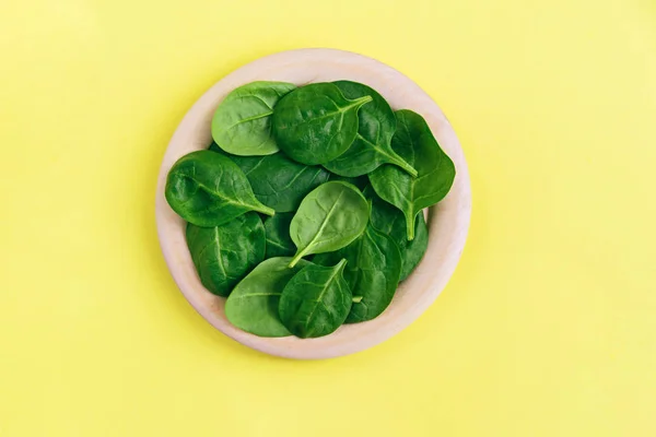 Green fresh vegetarian salad leaves on wooden plate on yellow background. — Stock Photo, Image