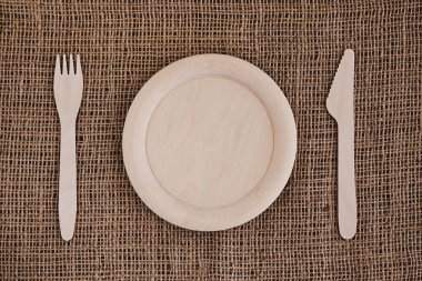 Tahta boş tabak, çatal ve bıçak çuval bezi arka planda. Sıfır atık.
