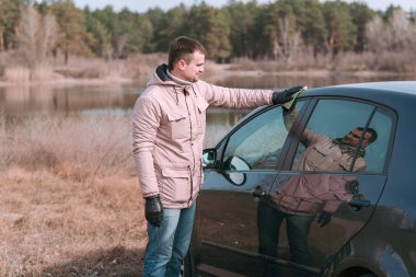 Genç yakışıklı adam sürmeden önce arabasını paçavrayla temizliyor..