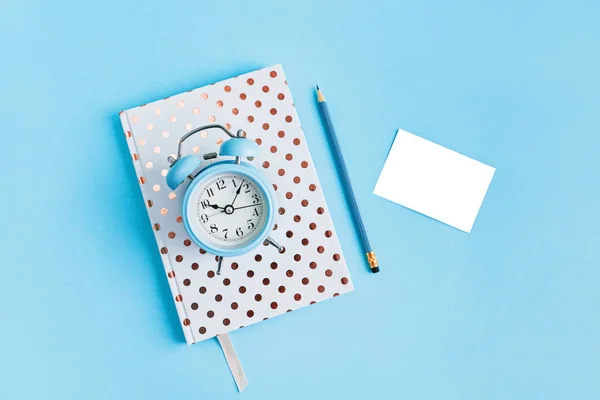 Cuaderno punteado blanco, pecil, despertador y papel blanco sobre fondo azul con espacio para copiar . — Foto de Stock