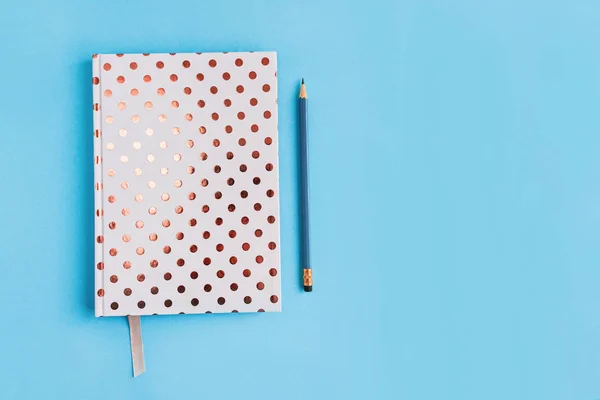 Cuaderno punteado blanco y pecil sobre fondo azul con espacio para copiar . — Foto de Stock